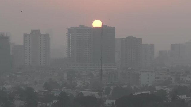 Tramonto in Karachi, Pakistan. Il sole scende rapidamente tra lo smog, dietro un palazzo con voli di uccello