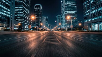 Fototapeta premium Illuminated skyscrapers tower over a motion-blurred road in a modern city center at night.