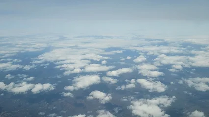 Aerial view above clouds with scattered formations over land, showing a serene sky scene with soft light and endless horizon, evoking a sense of freedom and peaceful travel. © UQink