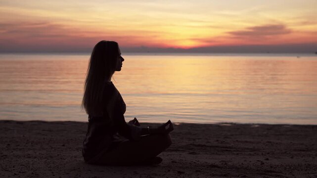 silhouette of a young women meditating by the sea at sunset, peaceful ocean background and warm light