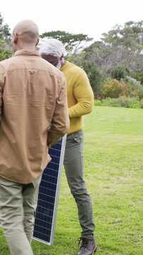 Vertical video: Arriving with solar panel, aide urging man in yellow sweater joining cables on lawn