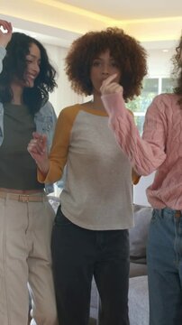 Vertical video: After head raise three women dancing at home by sofa, windows, central white raglan