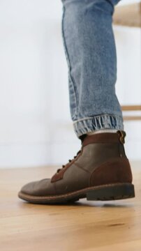 Vertical video: Shifting right leg in cuffed jeans, brown boot lifting heel and edging in studio