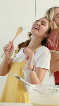 Vertical video: Grabbing spoon, overalls woman singing while red tee joining baking at home, bowl