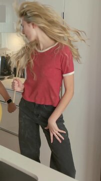 Vertical video: Dancing friends miming to music cue in kitchen with wooden spoons in red and yellow