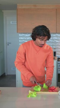 Preparing man in orange sweatshirt tearing lettuce, arranging tomato in kitchen with knife, ketchup