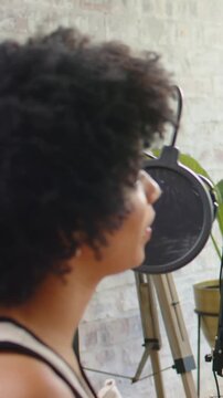 Vertical video: Singing woman leaning into mic in recording room after camera pan, sleeveless tank