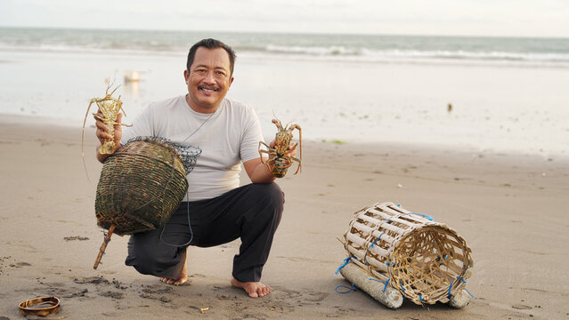 balinese fisherman with two lobsters in tabanan, bali, indonesia, caught at sea using traditional bamboo trap or pot, indonesian people, portrait smiling, looking at camera