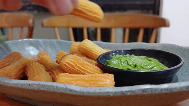 Close-up of a hand dipping a crispy golden churro into a bowl of green matcha paste. Sweet Spanish snack dessert served for delicious food experience video.