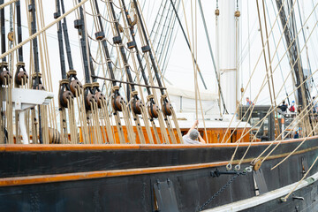 The crew is busy adjusting the rigging on a tall ship. They are on the deck, surrounded by ropes and pulleys. The sky is cloudy and other boats are in the background. © Videophilia