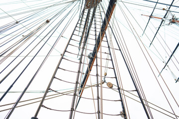 Obraz premium A person climbs the rigging of a tall ship. The scene shows many ropes and lines. The activity takes place high above the deck during daylight. The sky is clear and bright.