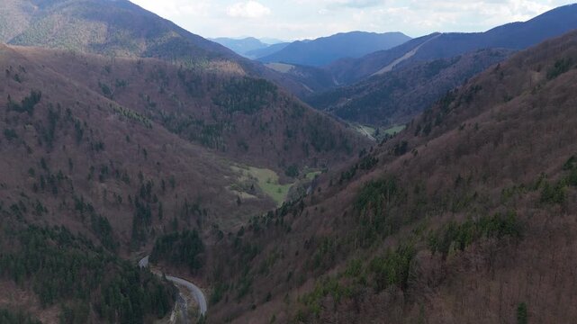 Aerial Drone Video Slowly Flying Forward Over Deep Mountain Valley with Winding Road in Early Spring