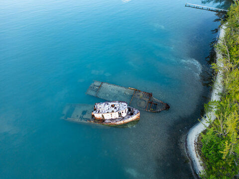 Aerial view of a rusty shipwreck submerged in clear turquoise water near a lush green shoreline in Guanaja, Bay Islands Department, Honduras.