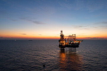Obraz premium Aerial view from a drone of big jack up offshore drilling oil rig, production platform and supply vessel In the ocean during sunset - Oil and Gas Industry