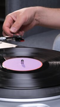Vertical video hand carefully lowering the stylus onto a spinning black vinyl record, playing music on a classic turntable for a vintage audio experience