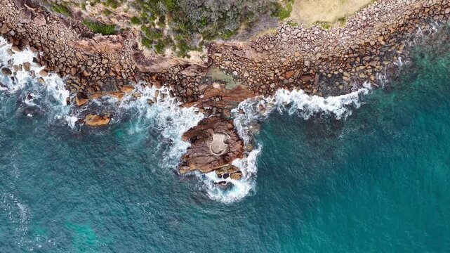 Aerial drone video of waves crashing onto rocky coastline surrounding World War II gun emplacement at Tomaree Head in Port Stephens, New South Wales, Australia.