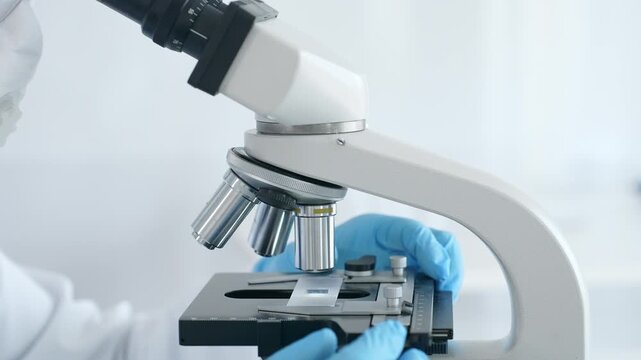 Close up of scientist's hands in blue gloves adjusting microscope in laboratory, conducting scientific research and analysis. Health care and science concept