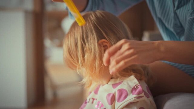 At home, a tender moment unfolds as a young mother gently combs her little daughter's hair with a small comb, fostering a sense of closeness and care in their quiet domestic routine