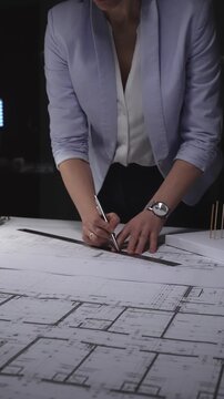 Architect drawing on construction plans, developing a new building design with a ruler and pen on paper. Architecture and business concept in low key lighting