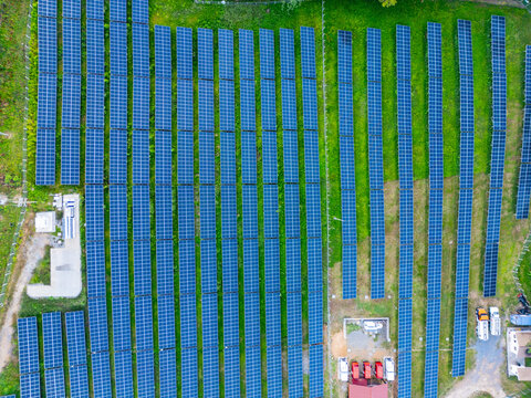 Aerial view of a large solar panel array with rows of blue photovoltaic modules surrounded by lush green grass and utility buildings in Guanaja, Bay Islands Department, Honduras.