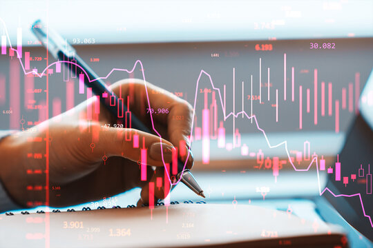 Hand noting financial data with glowing market charts and currency graphs overlayed in abstract business setting showing analysis and trends.