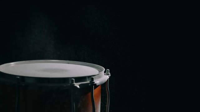Slow motion close up of drumstick striking snare drum causing dust particles to burst in dark studio