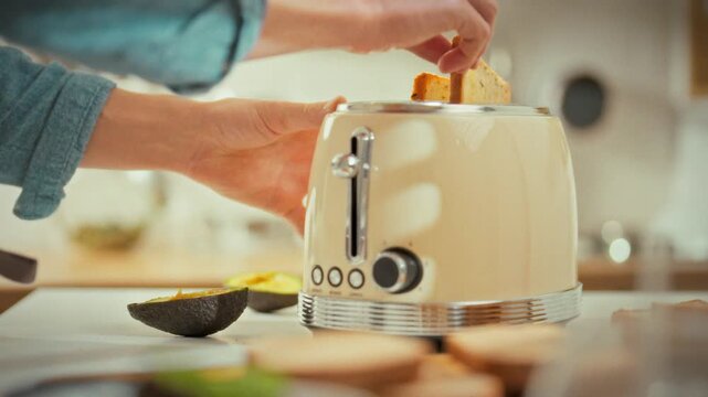 In kitchen, man's hands pull the toaster lever down, causing the hot toast to spring up. Freshly browned bread lands on the plate, ready for quick breakfast, highlighting the simple morning routine