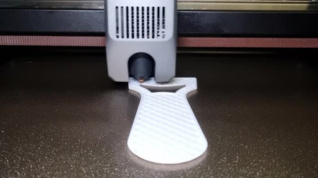 Compact white 3D printer extruder depositing filament to form a small curved object on a textured build plate.