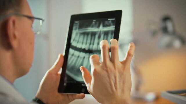 Examining high-resolution tablet, dentist studies panoramic image of patient's teeth, pinpointing each tooth, root and overall jaw health, showcasing modern dental technology for precise diagnosis
