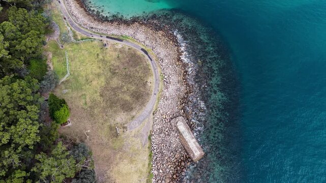 Aerial downward video of World War II torpedo emplacement on rocky coastline of Tomaree Mountain in Port Stephens, New South Wales, Australia surrounded by turquoise waters.