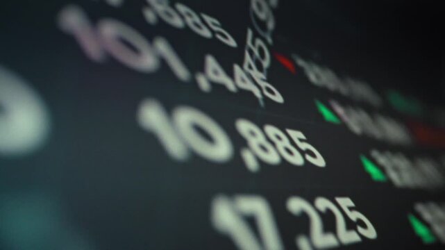 A finance monitor displays real-time stock market data fluctuating prices, exchange rates, and indices. An investor reviews current quotes and market trends on the screen