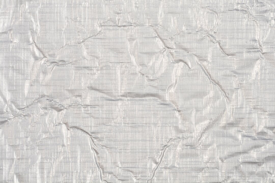 A macro shot of a thin silver aluminum foil featuring a crumpled texture and a fine embossed grid pattern on a reflective metallic surface