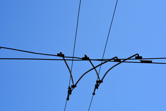 A low angle shot shows the complex network of metal cables and junctions for a tram overhead power system under a clear blue sky