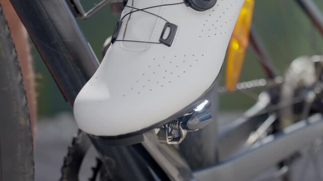 Cyclist clipping white road cycling shoe into clipless pedal on bicycle. Concept of endurance sport training and healthy lifestyle.