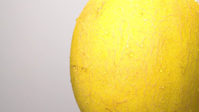 Close-up shot of a partial ripe yellow cantaloupe melon with tiny water droplets, rotating on a minimalist white background.