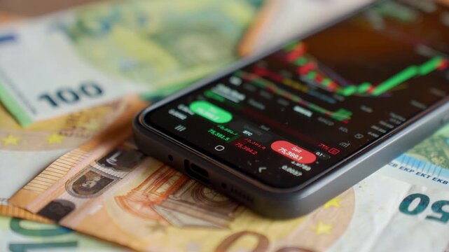 Smartphone showing trading app with market chart on euro banknotes. Concept of online investment financial risk mobile trading and digital finance.