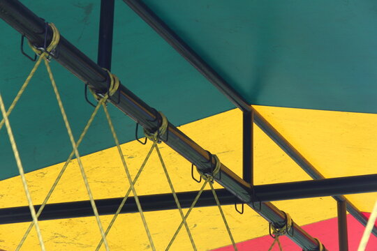 Close-up of a black metal frame structure with yellow ropes securing a vibrant multi-colored fabric canopy. Concept of industrial design, event infrastructure, safety, and construction details.