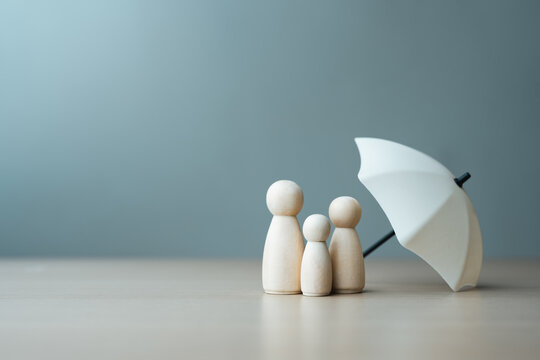 Wooden family figures protected by umbrella symbolizing health insurance, medical care, and financial protection, representing safety, coverage, and family security in healthcare concept.