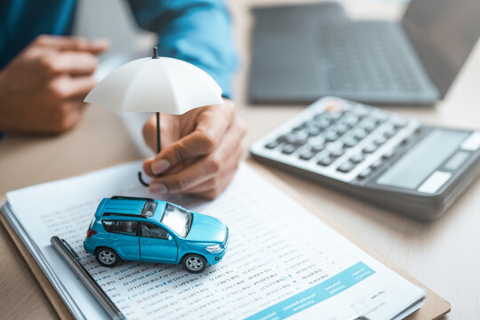 Insurance agent protecting car model with umbrella, representing auto insurance, financial protection, risk management, and coverage in modern business concept.