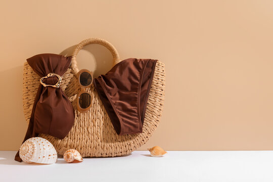 Wicker bag with brown swimsuit, sunglasses and seashells on color background