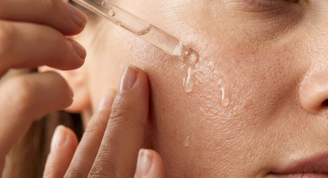 Smiling woman applying facial moisturizer serum from cosmetic pipette on facial skin. Skincare routine and wellness.
