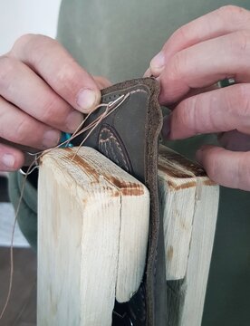 Close-up of a man's hands sewing a leather belt.