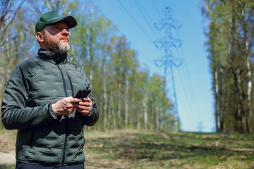 Fototapeta premium Forestry engineer. Ecologist conducts an inspection near power line pylons and records the data on their smartphone. Inspecting the power grid in the forest. 