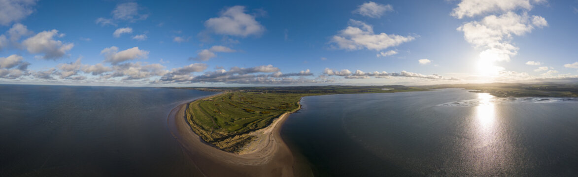 Aerial view of the historic golf links and sandy coastline under a bright sun and blue sky in St Andrews, Scotland, United Kingdom.