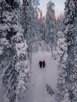 Amidst a winter wonderland, two travelers stroll through Akaslompolo, surrounded by towering snow-covered trees. Akaslompolo, Lapland Finland