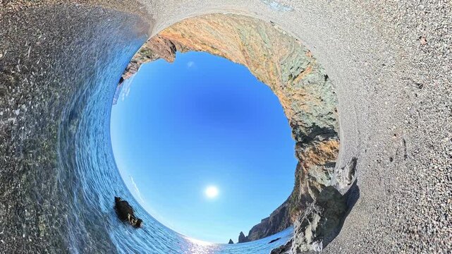 Ocean beach coastline captures a rocky shore and turquoise water under the bright sun using a unique immersive spherical perspective