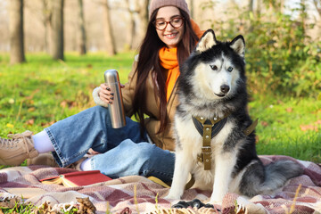 Beautiful young woman having picnic with cute husky dog in autumn park © Pixel-Shot
