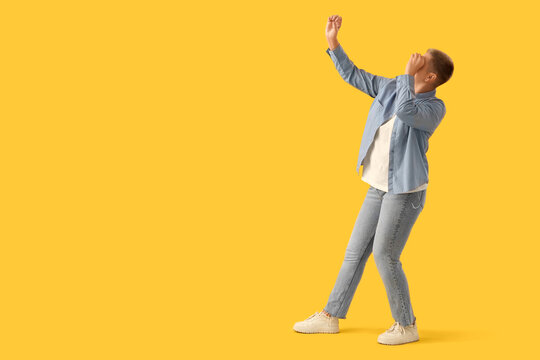Young woman looking through imaginary telescope on yellow background