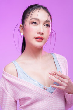 Beautiful young Asian woman with glowing skin and trendy wet hair look posing against a pastel pink background; elegant fashion portrait showcasing skincare, facial treatment, and Gen Z aesthetic.