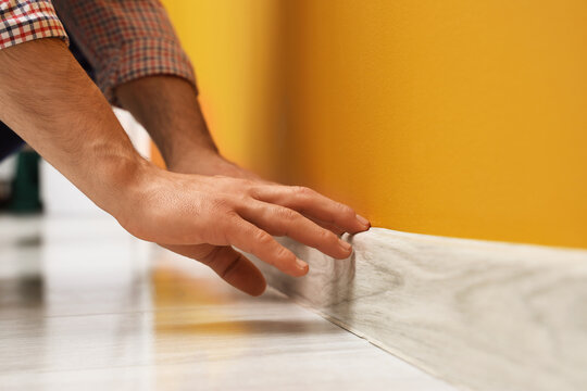 Worker installing beautiful wooden plinth on wall in stylish room, closeup